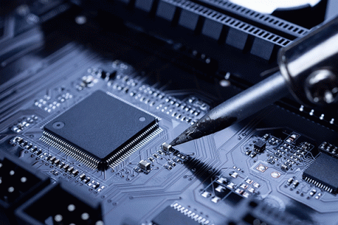 Close-up image of a dark grey computer chip in the panel of a computer, with a dark, pointed metal tool touching it. 